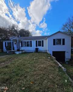 A white single-story house with black shutters and a ramp leading to the front porch sits on a sloped lawn at 425 Rollins Avenue in Henderson. A driveway leads to a garage under the right side. The sky is partly cloudy.