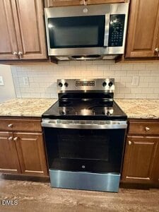 A stainless steel electric stove with a glass cooktop is positioned below a stainless steel microwave. Both appliances are set against a white subway tile backsplash and surrounded by brown wooden cabinets.