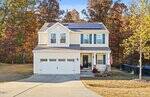 Charming two-story tan house with white trim and solar panels on the roof at 111 Richmond, featuring a spacious two-car garage, front porch with potted plants, an American flag, and surrounded by autumn trees and a grassy yard in the heart of Stem.