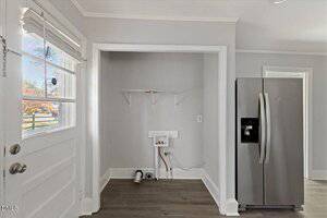 A laundry nook with washer and dryer hookups, a white wire shelf above, next to a stainless steel refrigerator and a back door with window. The room has light gray walls and wood flooring.