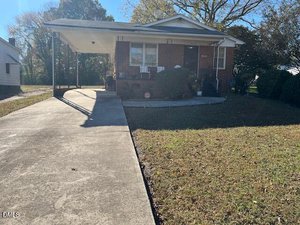 A single-story brick house in Henderson at 628 Farrar Avenue features a covered carport, concrete driveway, front porch with railing, and a grassy yard. Trees and shrubs are visible in the background under a clear sky.