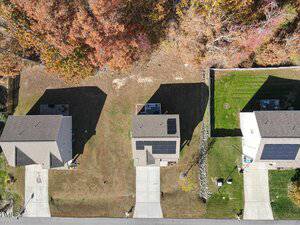 Aerial view of three houses with driveways, lawns, and solar panels on the roofs. Shadows from trees cover parts of the yards, and autumn foliage is visible along the top edge of the image.