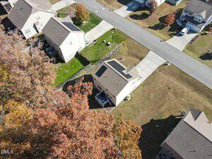 Aerial view of a suburban neighborhood showing several houses with driveways and lawns, a road running horizontally, and trees with autumn foliage in the foreground.