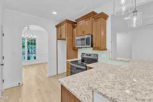 A modern kitchen with light wood cabinets, stainless steel appliances, granite countertops, glass pendant lights, hardwood floors, and an adjacent dining area with a large window and a chandelier.