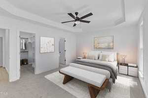 A modern bedroom with a large bed, bench, two bedside tables with lamps, a ceiling fan, artwork on the wall, and an open walk-in closet with shelves and hanging clothes. Neutral tones and soft lighting are used throughout.