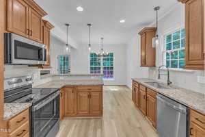 A modern kitchen with wood cabinets, granite countertops, stainless steel appliances, a double oven, a microwave, and a dishwasher. Large windows provide natural light, and pendant lights hang over the island.