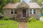 A small stone house at 630 E Avenue in Henderson with a front porch, stone steps, and a wooden door. Two chairs sit on the porch, flanked by plants along the steps, and a green lawn surrounds the home.