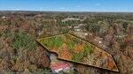 Aerial view of a wooded property on 0 Ridgecrest Lane in Henderson, outlined in orange, surrounded by autumn trees with houses and buildings scattered nearby in a rural area under a blue sky.