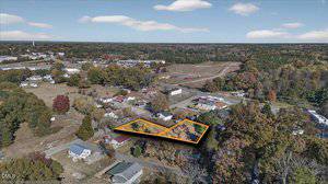 Aerial view of a small residential area with houses, roads, and trees in autumn. A specific property with two wooded lots is outlined in orange near the center lower part of the image.