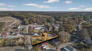 Aerial view of a small rural town with houses, trees with autumn foliage, and a marked area outlined in orange highlighting two adjacent lots. Roads and scattered buildings surround the marked property.