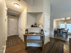 A hallway in a home with white doors, wood flooring, and a wooden console table decorated with lanterns and small items. An adjacent dining room with a table and chairs is visible to the right.