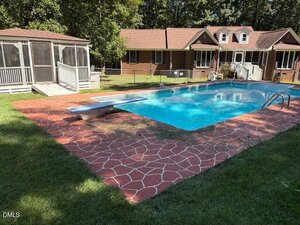 Rectangular outdoor swimming pool with a diving board and red stone-patterned pool deck at 80 White Deer Lane, Henderson. Surrounded by grass, with a screened porch and brown house with white trim in the background.