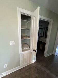 A small closet in a light green wall, with the door open to reveal three shelves lined with a protective covering. An air vent is located at the bottom of the closet. The adjacent room is partially visible.