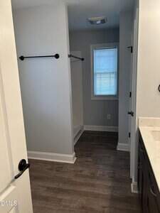 A bathroom with gray walls, dark wood flooring, a white shower stall with black towel bars, a window with blinds, and a white countertop with a dark vanity cabinet.