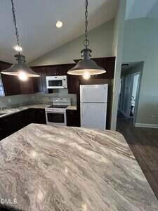 A modern kitchen with dark wood cabinets, white appliances including a refrigerator, stove, and microwave, marble-patterned countertops, and two pendant lights hanging above the counter.