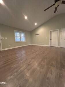 An empty room with light green walls, wood flooring, recessed lighting, a ceiling fan, a large window, and two white doors on the right-hand wall.