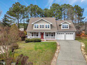 Charming two-story suburban house at 105 Byron Court, Oxford, with gray siding, white trim, a covered porch, and double garage. Curved driveway leads to a yard with shrubs and grass, bordered by tall pine trees in the background.