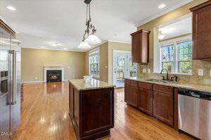 Open-concept kitchen and living area with hardwood floors, dark wood cabinets, stainless steel appliances, a large window, and a fireplace in the living room. Glass doors lead to an outdoor deck.