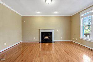 Empty living room with light brown walls, a white ceiling, wood floors, a fireplace centered on the far wall, and a large window on the right letting in natural light.