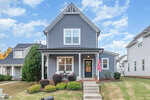 A two-story gray house with white trim at 203 Kipling Drive, Oxford, features a front porch with white railings, a wreath on the door, an American flag, and neatly trimmed shrubs. Steps lead from the sidewalk to the welcoming porch.