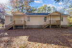 A single-story beige house at 691-693 Boddie Street in Henderson features two wooden porches, each with steps to separate entrances, set on a lot covered with dry leaves and surrounded by trees on a sunny day.