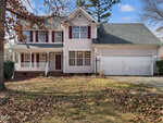 A two-story suburban house at 2035 Ferbow Street, Creedmoor, features light-colored siding, dark shutters, a covered front porch, and a double garage. Fallen leaves cover the lawn and driveway; trees with sparse leaves surround the property.