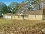A single-story beige house at 3182 Sims Bridge Road in Kittrell features a covered front porch and a detached three-car garage, surrounded by trees and a lawn covered in brown fallen leaves.