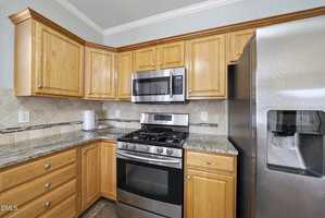 A kitchen corner features wooden cabinets, granite countertops, a stainless steel gas stove with an oven, a microwave above it, and a stainless steel refrigerator with a water and ice dispenser.