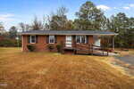 Charming single-story brick house at 606 29th Street, Butner, with black shutters, a covered carport on the right, and a wooden wheelchair ramp. The home sits on a large grassy lot with trees in the background.