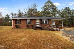 Charming single-story brick house at 606 29th Street, Butner, with black shutters, a covered carport on the right, and a wooden wheelchair ramp. The home sits on a large grassy lot with trees in the background.