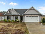 A single-story gray house with white trim and a black roof at 103 Averly Court, Stem. This home features a two-car garage, manicured shrubs, patchy front lawn, concrete driveway, and a walkway leading to the entry door.