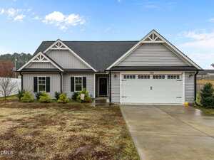 A single-story gray house with white trim and a black roof at 103 Averly Court, Stem. This home features a two-car garage, manicured shrubs, patchy front lawn, concrete driveway, and a walkway leading to the entry door.