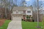 Two-story Wake Forest suburban house with stone and siding exterior, attached two-car garage, red front door, and covered porch. Located at 1321 Sourwood Drive, it features a lawn and is backed by tall leafless trees.