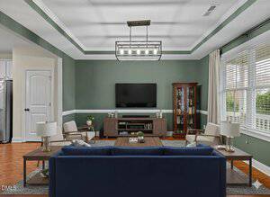 A living room with green walls, a blue sofa, two beige chairs, a wooden TV stand with a flat-screen TV, a glass-front cabinet, two side tables with lamps, and large windows with white blinds.