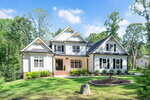A large two-story white house with black trim and multiple gables sits on a green lawn at 3511 Bruce Garner Road, Wake Forest, surrounded by shrubs, a circular stone feature, and trees under a blue sky.