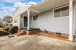 A single-story house with light blue siding, a covered front porch with green flooring, red brick steps, and a white pillar. The house number 109 is visible near a window. There is a concrete driveway in front.