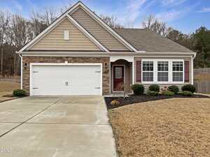 Single-story suburban house at 2726 Spring Valley Drive in Creedmoor, featuring a two-car garage, stone and siding exterior, red front door, multiple front windows, manicured lawn, trimmed shrubs, driveway, and welcoming walkway to the entrance.