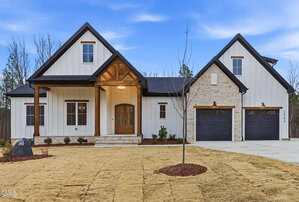 A modern farmhouse-style home in Youngsville at 3904 Cedar Knolls Drive, featuring white siding, stone accents, wood trim, two front-facing garage doors, a covered entry porch, and a freshly landscaped yard with sparse grass and young shrubs.