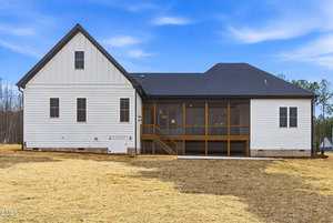 A modern white house with dark roof shingles, multiple windows, and a screened-in back porch with wooden stairs. The yard is covered with straw and the sky is mostly clear with some clouds.