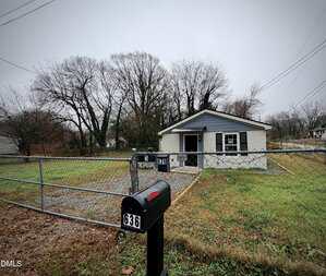 A small, single-story house with gray siding and white trim is behind a chain-link fence. A "No Trespassing" sign and the number 636 are visible on the fence and mailbox. The yard has patchy grass and leafless trees.