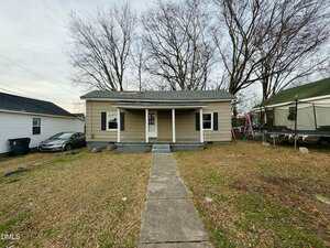 Charming single-story beige house with a gray roof at 316 Piedmont Avenue, Oxford. Features two front columns, a concrete walkway to the entrance, leafless trees behind, a car on the left, and a trampoline on the right.