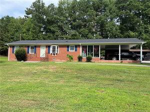 A single-story red brick house with black shutters, a white front door, and a covered carport attached on the right side sits at 1675 US 15 in Creedmoor, surrounded by a large grassy yard with trees in the background.