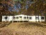 A single-story white house with black shutters sits in a wooded area at 4131 Morton Lane, Franklinton. The home features a central front porch with a wooden railing and steps, surrounded by trees with autumn leaves on the ground.