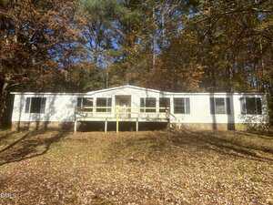A single-story white house with black shutters sits in a wooded area at 4131 Morton Lane, Franklinton. The home features a central front porch with a wooden railing and steps, surrounded by trees with autumn leaves on the ground.