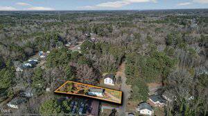 Aerial view of a residential area surrounded by trees. A single property with a house and driveway is outlined in orange, highlighting its boundaries within the neighborhood. Other homes and roads are visible nearby.