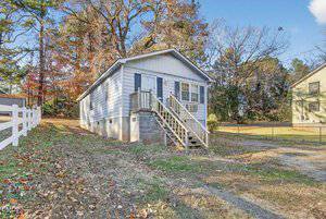 A small, light gray house with white trim sits raised on a cinder block foundation at 426 Thomas Street, Henderson. Wooden steps lead to the front door. The sloped yard features scattered leaves, a gravel driveway, and trees in the background.
