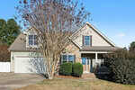 This two-story suburban house at 1731 Riverstone Drive in Franklinton features a stone and beige exterior, a front porch, an attached two-car garage, trimmed bushes along the walkway, and a large leafless tree in the yard.