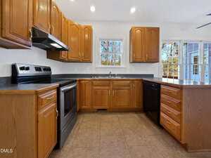 Kitchen with wooden cabinets, black appliances, tile flooring, and a double sink under two windows. Large counter space and French doors provide natural light and an outdoor view.
