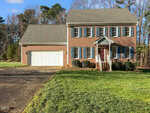 A two-story brick house on 2013 Pratt Circle in Franklinton with white trim, blue shutters, and a red front door features a double garage and a neatly mowed lawn, set against a backdrop of trees under a clear sky.