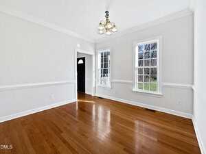 A bright, empty room with white walls, hardwood floors, a window letting in natural light, and a ceiling light fixture. There is a doorway leading to another area of the house.